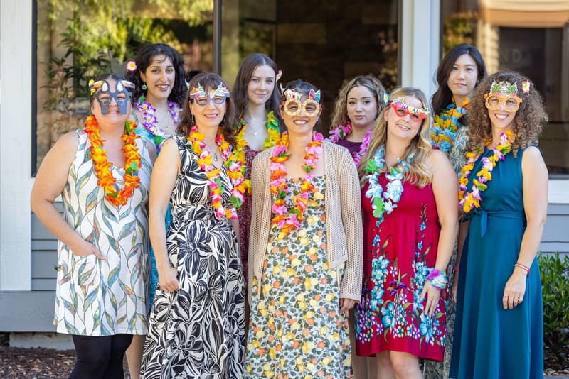 The team in flower leis and party glasses, smiling outside the office