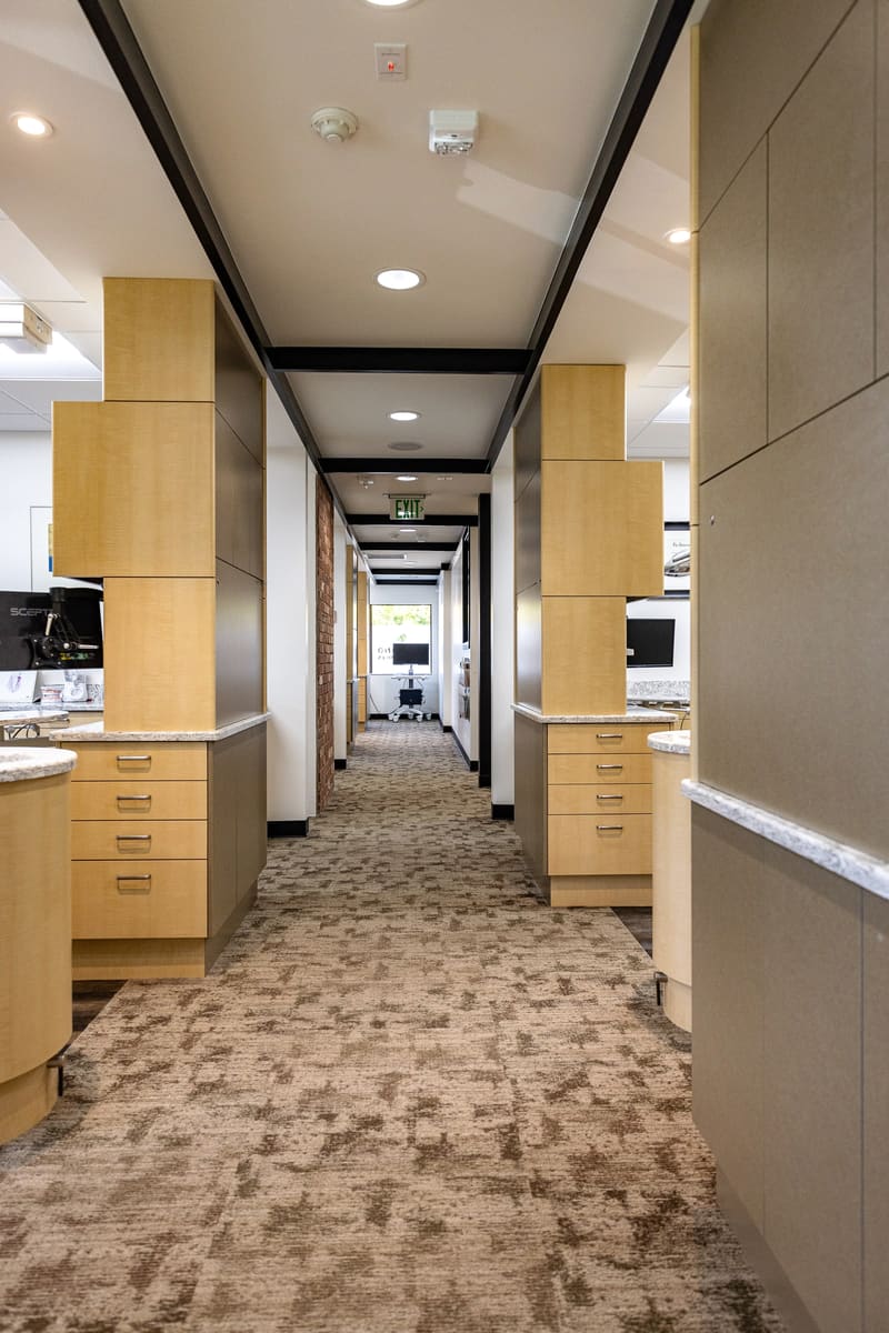 Hallway with light wood cabinetry and patterned carpet leading past the treatment rooms