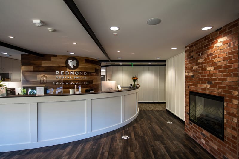 Reception desk at Redmond Dental Smiles with the practice logo on a reclaimed-wood wall and a brick fireplace
