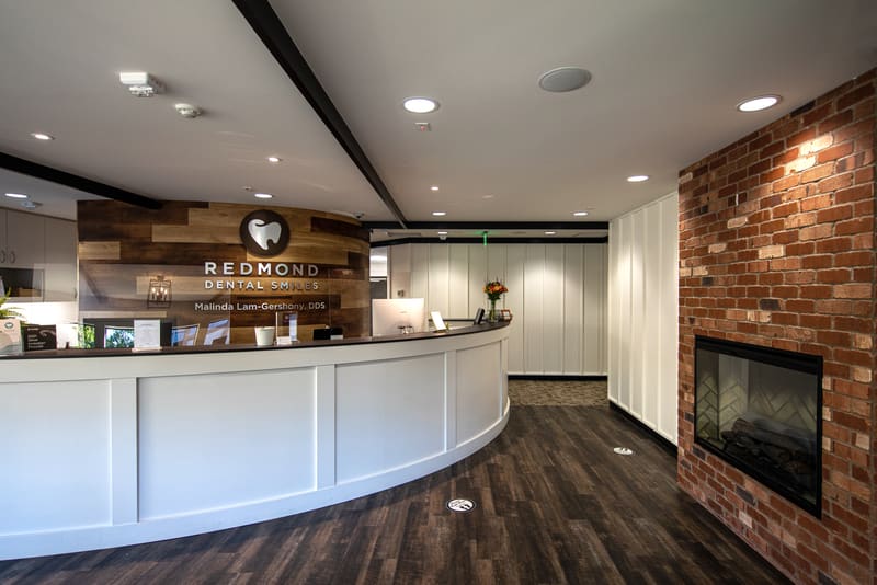 Reception desk at Redmond Dental Smiles with the practice logo on a reclaimed-wood wall and a brick fireplace
